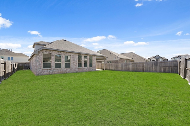 rear view of property featuring brick siding, a lawn, a fenced backyard, and roof with shingles