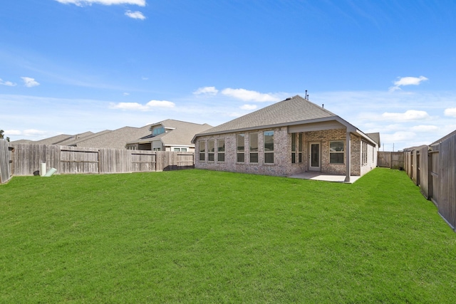 rear view of house with brick siding, a patio, a shingled roof, a lawn, and a fenced backyard