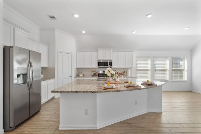 kitchen with appliances with stainless steel finishes, wood tiled floor, white cabinetry, and decorative backsplash