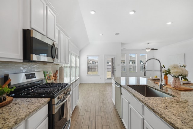 kitchen featuring stainless steel appliances, wood finish floors, a sink, white cabinetry, and decorative backsplash