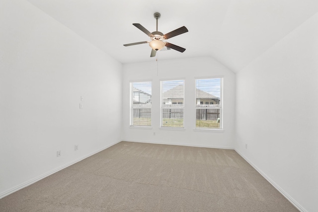 empty room featuring lofted ceiling, ceiling fan, baseboards, and light colored carpet