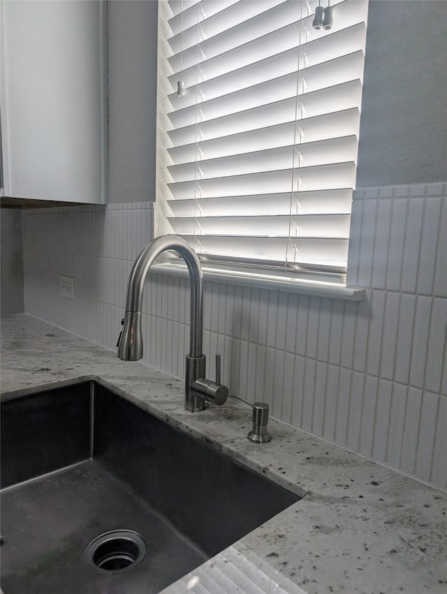 details featuring tasteful backsplash, a sink, and light stone countertops