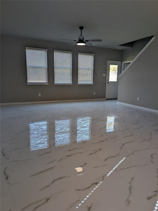 unfurnished living room with marble finish floor, ceiling fan, and baseboards