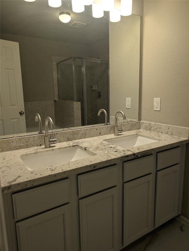 full bathroom with double vanity, a stall shower, visible vents, and a sink