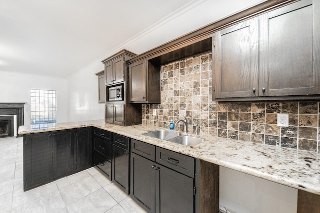 kitchen with a peninsula, a sink, backsplash, stainless steel microwave, and crown molding