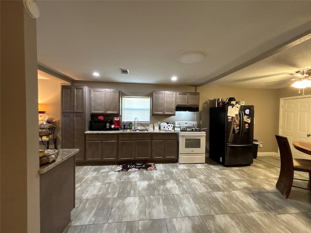 kitchen with white gas stove, visible vents, freestanding refrigerator, a sink, and under cabinet range hood