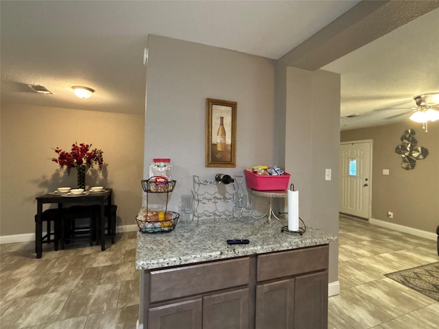 kitchen featuring light stone countertops, visible vents, baseboards, and ceiling fan