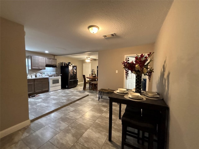 kitchen featuring white range with gas stovetop, baseboards, visible vents, freestanding refrigerator, and under cabinet range hood