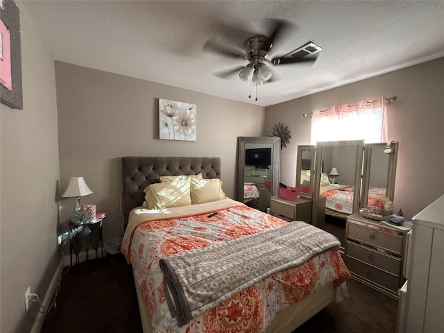 bedroom with visible vents, dark carpet, a textured ceiling, and ceiling fan