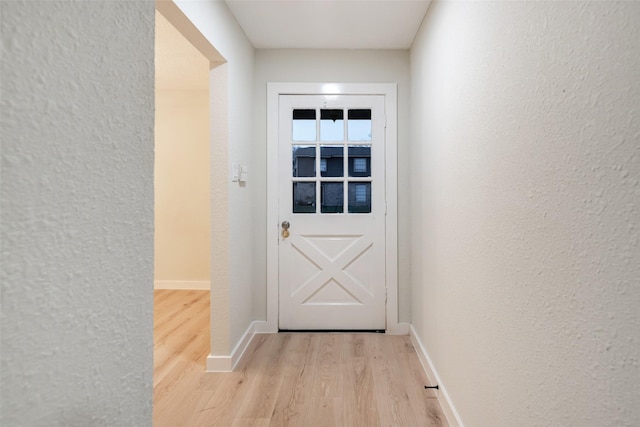 doorway to outside with light wood-style floors, a textured wall, and baseboards