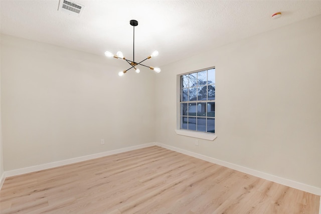 spare room with baseboards, visible vents, an inviting chandelier, a textured ceiling, and light wood-type flooring