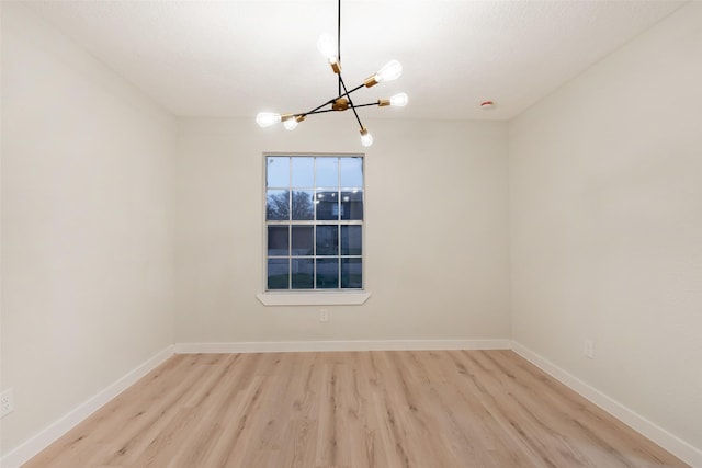 spare room featuring an inviting chandelier, baseboards, and wood finished floors