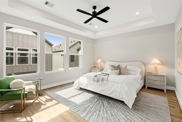 bedroom featuring baseboards, visible vents, a raised ceiling, wood finished floors, and recessed lighting