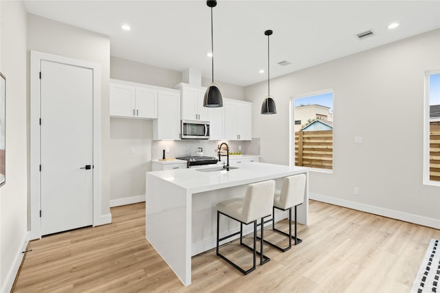 kitchen with visible vents, decorative backsplash, stainless steel microwave, light wood-type flooring, and a sink