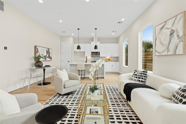 living area featuring baseboards, light wood finished floors, visible vents, and recessed lighting