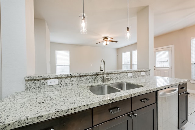 kitchen featuring light stone counters, pendant lighting, stainless steel dishwasher, a sink, and dark brown cabinets