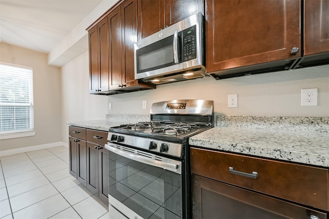 kitchen with light stone counters, light tile patterned floors, appliances with stainless steel finishes, dark brown cabinets, and baseboards