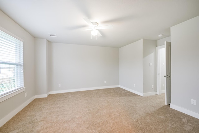 spare room featuring baseboards, ceiling fan, visible vents, and light colored carpet