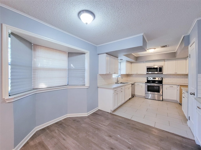 kitchen with stainless steel appliances, a sink, ornamental molding, backsplash, and light wood finished floors