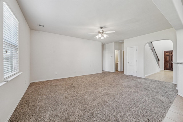 empty room with light carpet, light tile patterned floors, arched walkways, and a ceiling fan