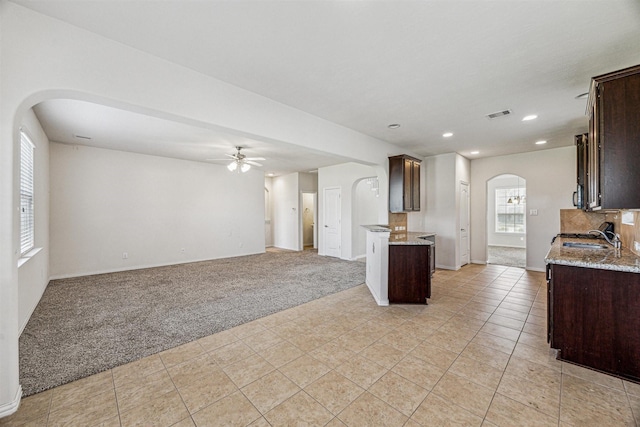 kitchen with arched walkways, dark brown cabinetry, light carpet, visible vents, and light stone countertops