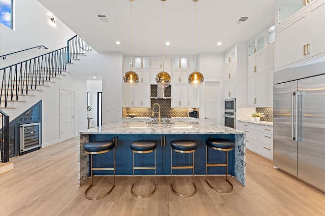 kitchen featuring light wood finished floors, visible vents, built in appliances, and a sink