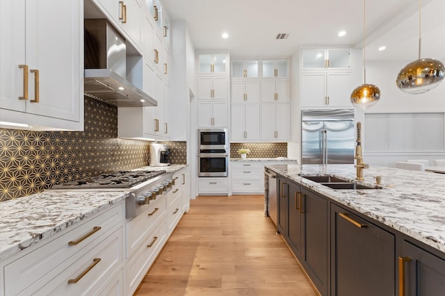 kitchen featuring white cabinetry, light wood finished floors, glass insert cabinets, built in appliances, and extractor fan