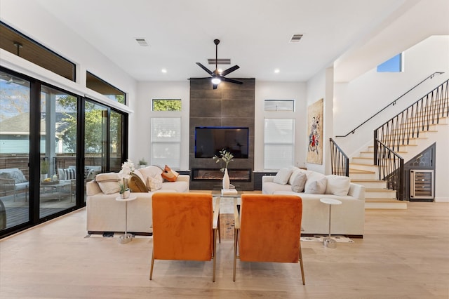 living room with visible vents, a tile fireplace, stairs, wine cooler, and light wood-type flooring