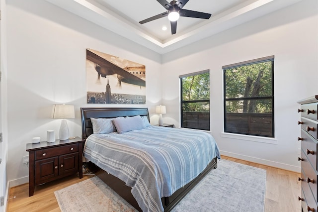 bedroom featuring light wood finished floors, recessed lighting, a raised ceiling, and baseboards