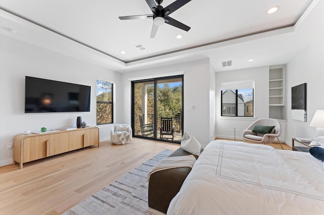 bedroom with light wood-type flooring, a tray ceiling, visible vents, and access to exterior