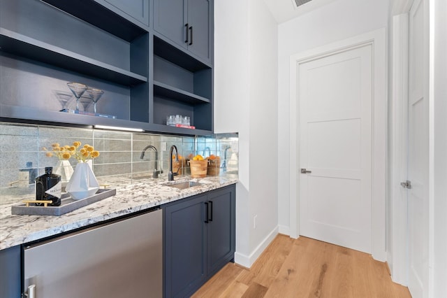 bar with a sink, baseboards, light wood finished floors, decorative backsplash, and wet bar