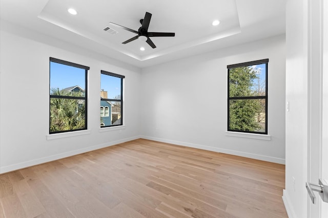 empty room featuring light wood finished floors, visible vents, a raised ceiling, and baseboards