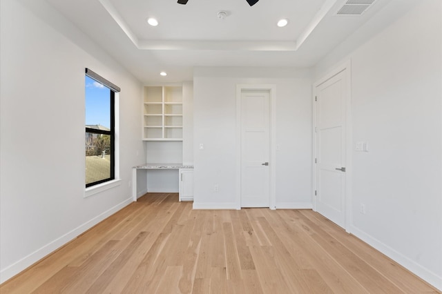 unfurnished bedroom featuring light wood finished floors, visible vents, baseboards, and a tray ceiling