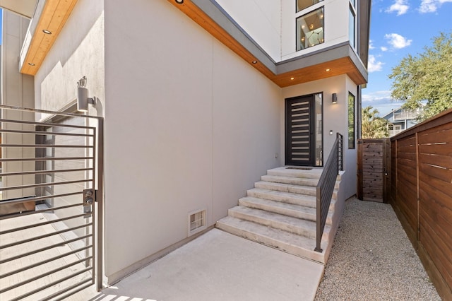 doorway to property featuring fence, visible vents, and stucco siding