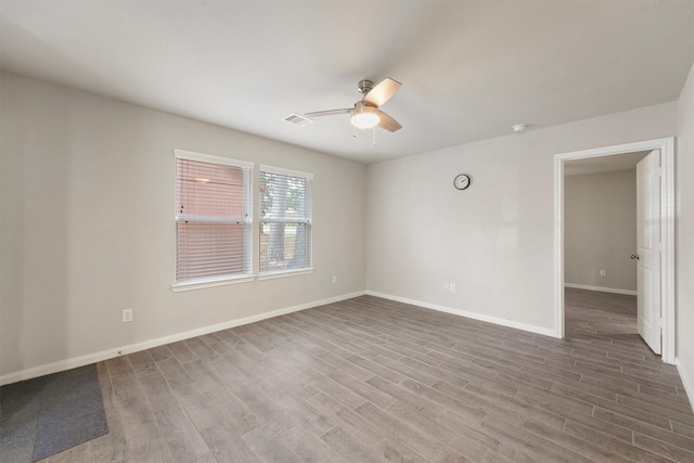 empty room featuring a ceiling fan, visible vents, baseboards, and wood finished floors