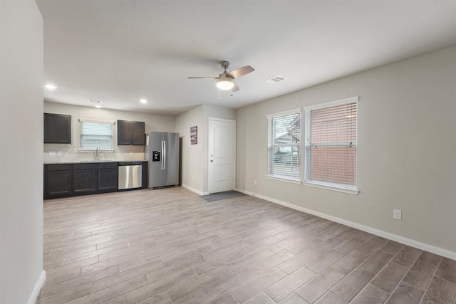 kitchen featuring appliances with stainless steel finishes, a ceiling fan, light wood-style flooring, and baseboards