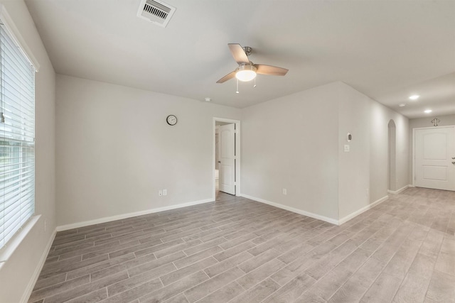 unfurnished room featuring light wood-style floors, visible vents, arched walkways, and a ceiling fan