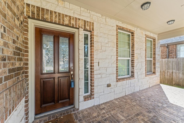 view of exterior entry featuring covered porch, brick siding, and fence