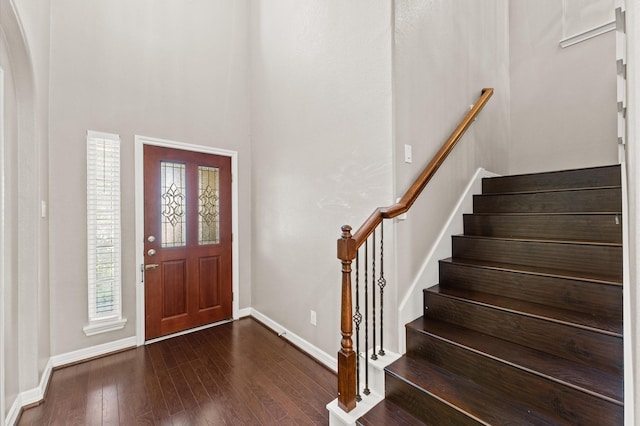 foyer entrance with dark wood-style floors, stairway, arched walkways, and baseboards