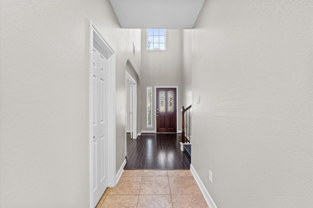 doorway with a towering ceiling, baseboards, and tile patterned floors