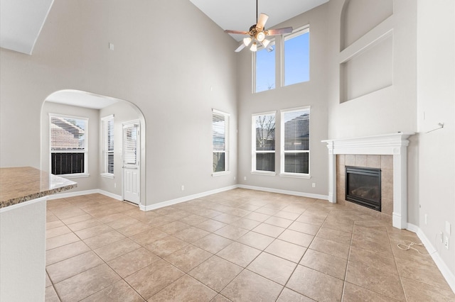 unfurnished living room with light tile patterned flooring, a fireplace, a ceiling fan, and baseboards