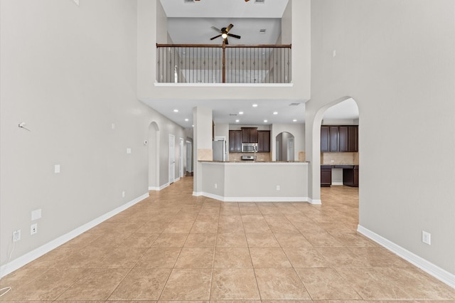 unfurnished living room featuring ceiling fan, arched walkways, baseboards, and light tile patterned flooring