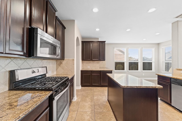 kitchen featuring dark brown cabinetry, a kitchen island, appliances with stainless steel finishes, and light stone counters