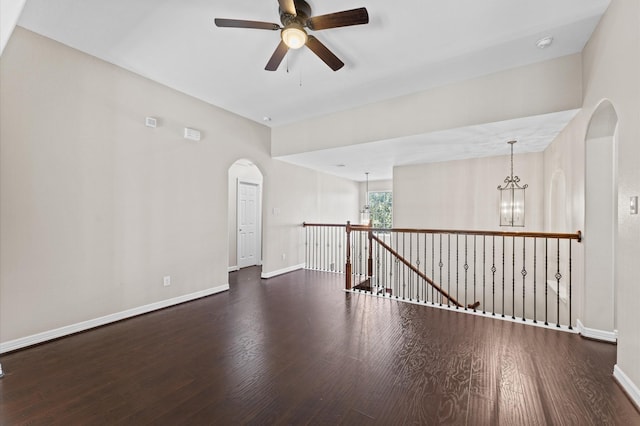 spare room featuring baseboards, arched walkways, wood finished floors, and ceiling fan with notable chandelier