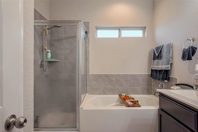 bathroom featuring a stall shower, a textured wall, a bath, and vanity