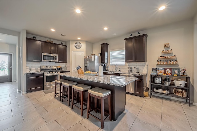 kitchen featuring appliances with stainless steel finishes, dark brown cabinetry, a breakfast bar area, and light stone countertops