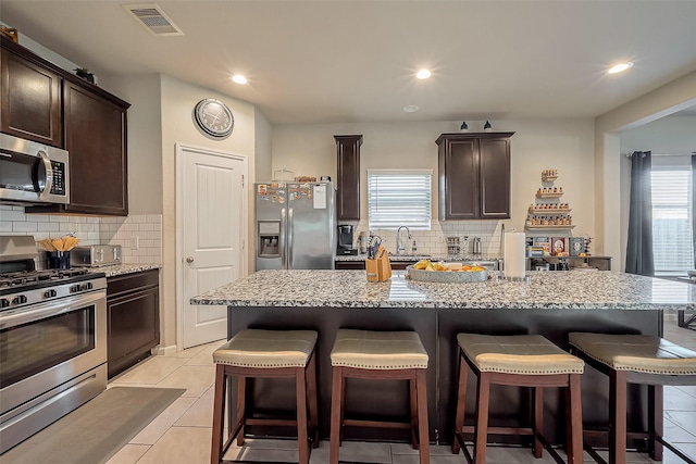 kitchen featuring stainless steel appliances, visible vents, dark brown cabinets, and a breakfast bar area