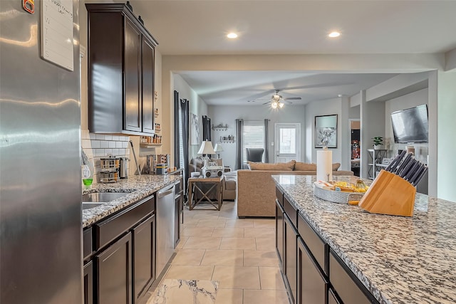 kitchen with open floor plan, stainless steel appliances, dark brown cabinets, and dark stone countertops