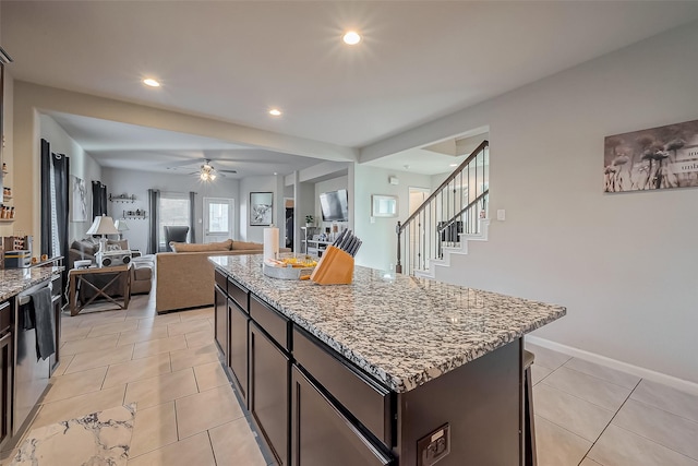 kitchen featuring dark brown cabinetry, light tile patterned flooring, light stone counters, and a center island