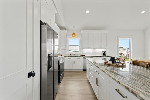 4214 Jackson Dr, Galveston, TX 77554 - kitchen featuring white cabinets, decorative backsplash, appliances with stainless steel finishes, light stone counters, and light wood-type flooring